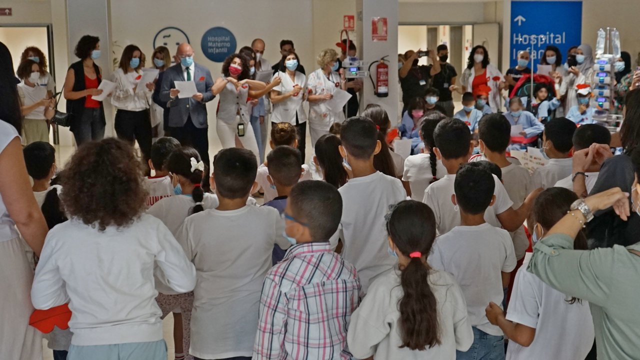 Los niños del CEIP Santa Rosa de Lima (de espaldas) cantan 'Un beso redondo' acompañados de familiares, personal del hospital, voluntarios, el gerente del SMS, Francisco Ponce, y la directora general de Asistencia Sanitaria, Isabel Ayala.