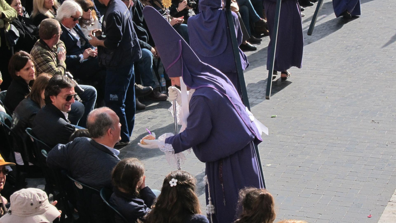Un nazareno entregando una mona a un conocido en la ma&ntilde;ana de Viernes Santo